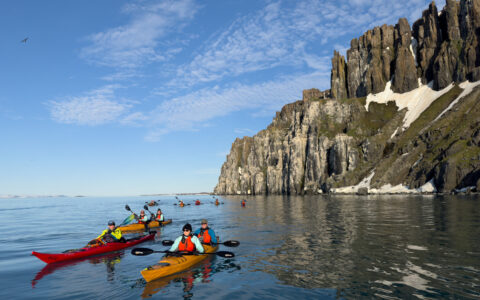 Red and yellow kayaks in the calm seas off the steep snowy cliffs