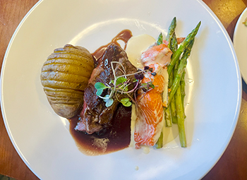 Baked potato and steak alongside salmon and asparagus served over sauces on a white plate.