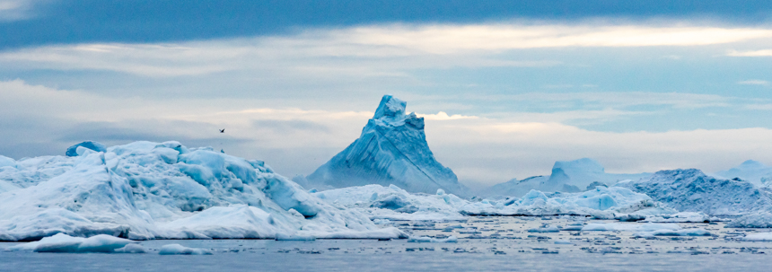 white and blue iceberg floating in the ocean with mountains in the background