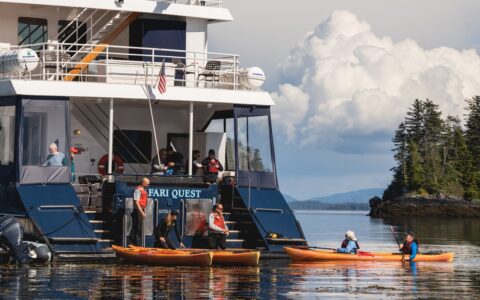 The safari quest Alaska small ship floats as guests return from a kayak activity, the crew on board waiting to help them disembark.