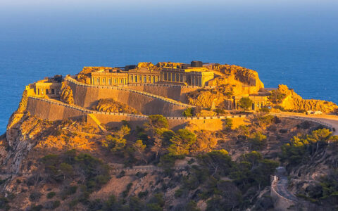 A coastal artillery fortification, known as Batería de Castillitos, built into a rocky cliffside with a clear blue sky in the background.