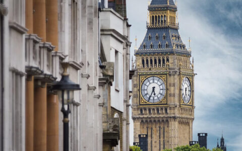 A close-up view of the Elizabeth Tower, also known as Big Ben, with its clock face visible, and a part of the Houses of Parliament building to the left.