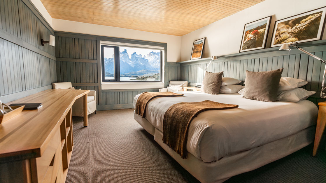 Large bed, wooden desk & chair, views to water & mountains from Cordillera Paine Room at Explora Torres del Paine Lodge in Chile.