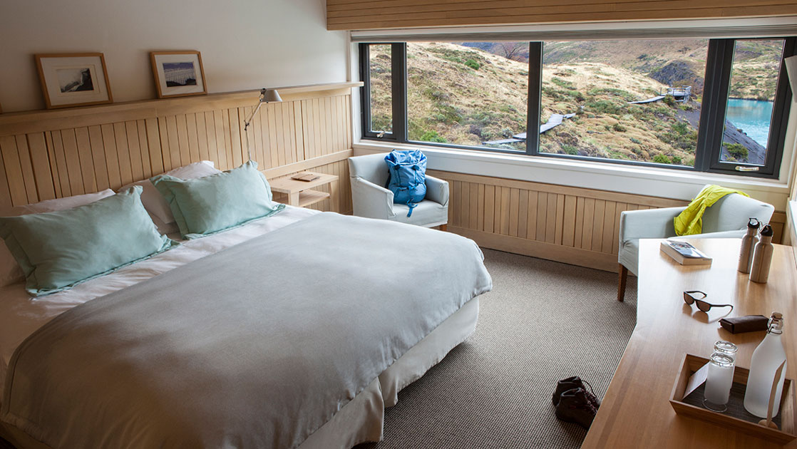 Salto Chico Room at Explora Torres del Paine Lodge, with large double bed in white linens, wood beadboard, desk & view window.