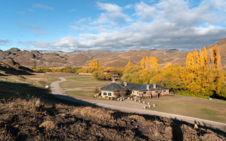 Aerial view of small stone wilderness lodge sitting in Patagonia National Park valley with yellow-leaf trees under some clouds.