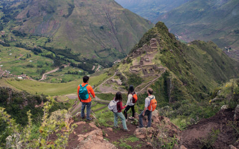 4 Explora Sacred Valley travelers in bright clothes stand atop an outcrop looking down onto Machu Picchu on a hazy day in Peru.