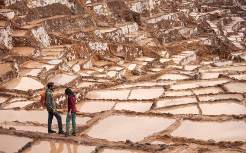 2 young, adult Explora Peru Sacred Valley travelers stand among terraced square salt mines.