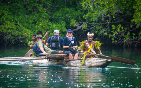 Frontier Lands of New Guinea cruise guests ride in a wooden carved canoe paddled by native locals in celebratory dress.