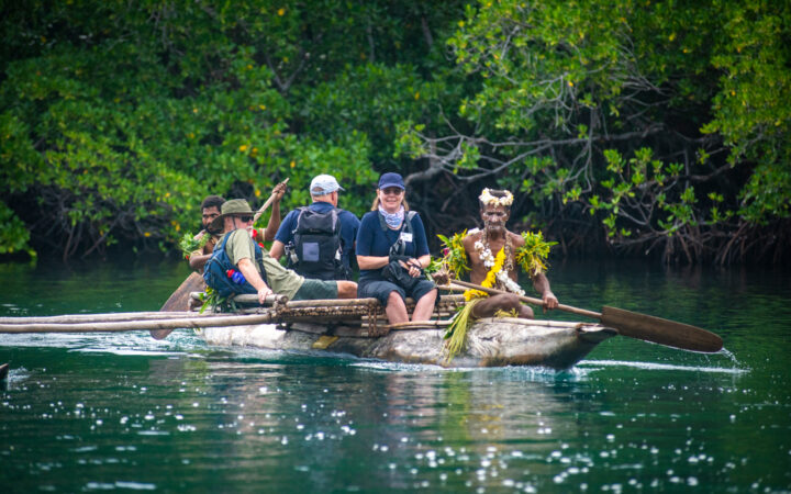 Frontier Lands of New Guinea cruise guests ride in a wooden carved canoe paddled by native locals in celebratory dress.
