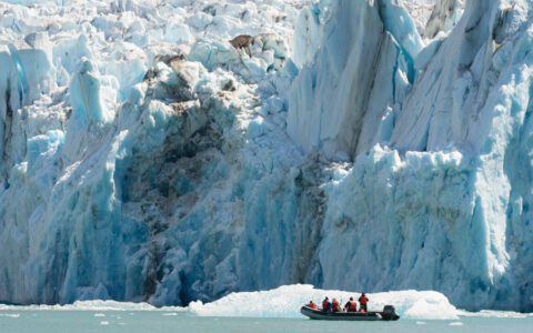 Small skiff filled with adventurer's exploring massive icebergs and glaciers on bright sunny day in Alaska