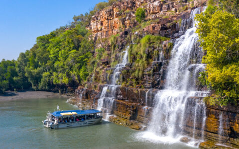 Silver Xplorer tender boat pulls up in front of cascading waterfalls under a blue sky in Australia's Kimberley Region.