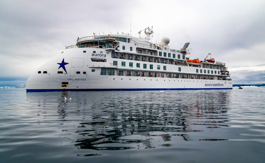 Aurora small cruise ship with an x bow and white paint with blue accents and a blue star on the bow and 5 decks