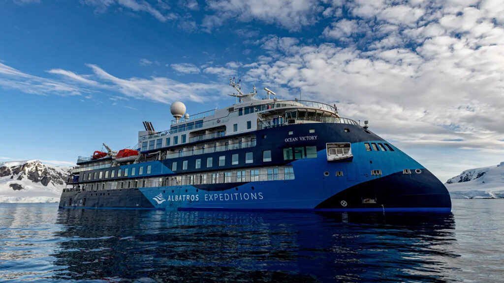 blue and white polar expedition ship Ocean Victory cruising through the icy waters of Antarctica on a sunny calm day