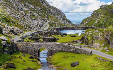 A scenic view of the Gap of Dunloe in County Kerry, Ireland, showing a narrow mountain pass with a road running through a valley, rocky hillsides.