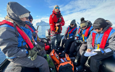 Zodiac boat with Antarctica travelers dressed warmly as they collect citizen science samples on a sunny day.