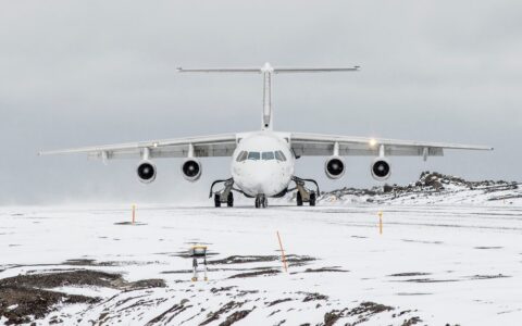 A white snowy landscape on a overcast day, a white charter plane sits on an empty runway ready for Antarctica Air cruises.