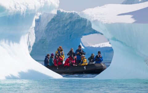 A zodiac full of guests from the antarctica air cruise passes in front of a pyramid shaped iceberg