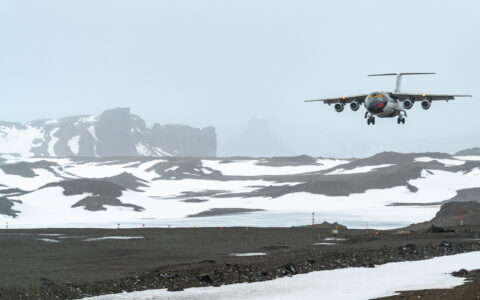 Small jet painted like a macaroni penguin comes in for a misty landing on a gravel airstrip among snowdrifts in Antarctica.