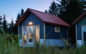 Cabin at dusk at Bear Camp Alaska with a red roof, large windows with a glass door