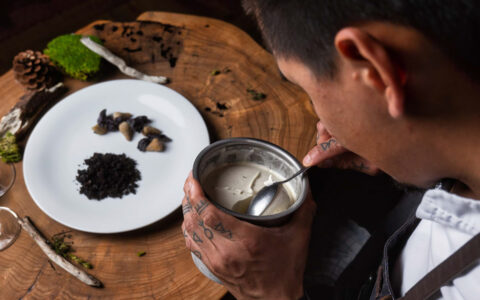 Man stirs cream beside plate with foraged Arctic food sitting atop a tree stump table during a Gems of West Greenland cruise.