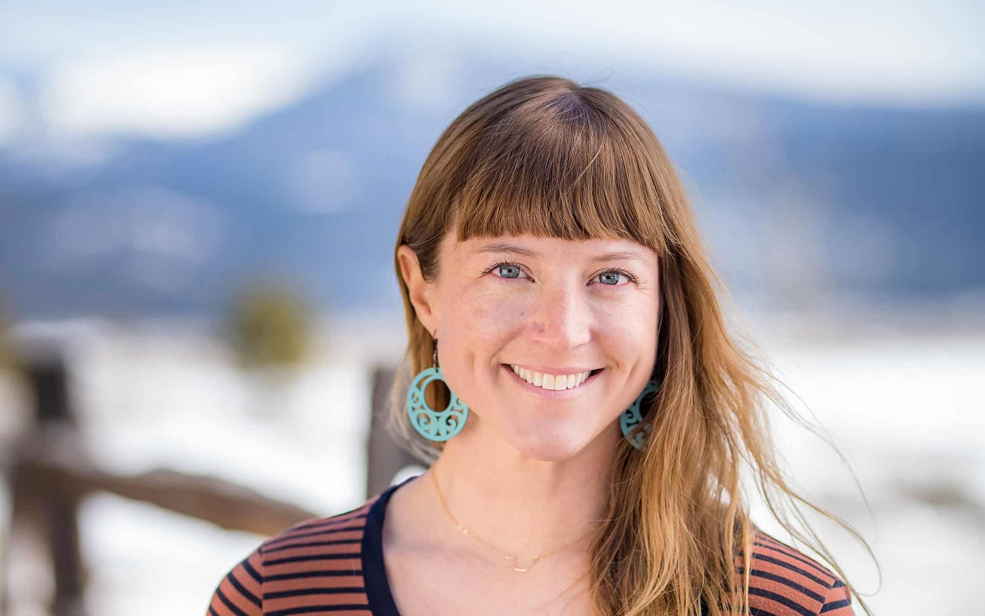 adventuresmith explorations director of content and marketing lis korb wearing a striped shirt smiling with snow and mountains behind her