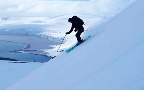 A backcountry skiier makes turns down a steep slope in Antarctica, on a cloudy day.