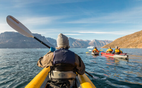 View from behind front paddler in inflatable yellow tandem kayak on a sunny day on an Under The Northern Lights Arctic cruise.