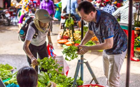 Travelers with chef David Thompson shopping for fruits and vegetables at the local outdoor market.