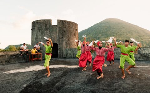 Dressed in bright red and green traditional clothing boys and girls dance, spinning white handkerchiefs during a performance at Fort Belgica in Indonesia.