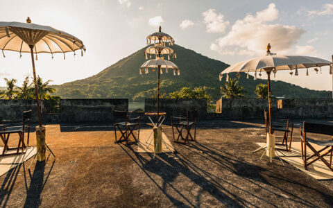 White parasols with gold tassels cover empty director's chairs at by a green hillside on the roof of Fort Belgica at sunset.