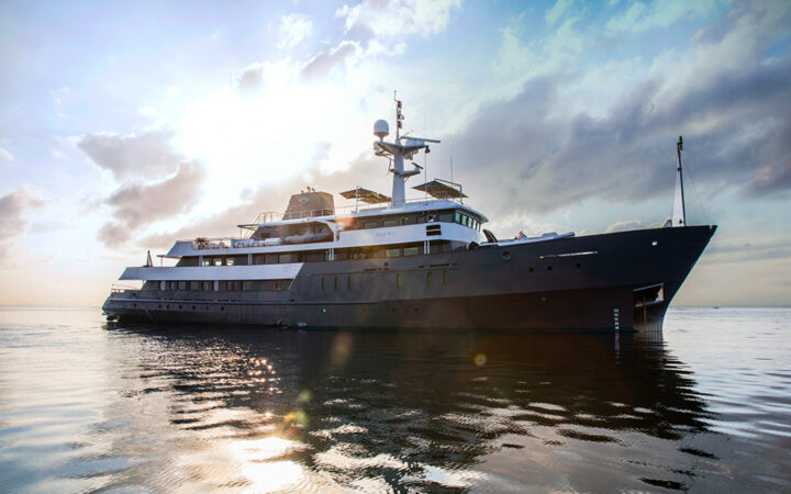 blue ship in open water with bright clouds and sun peaking through