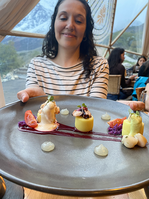 A woman in striped shirt holds up a black plate of food at EcoCamp Patagonia