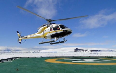 A helicopter lands on a pad surrounded by ice in antarctica, as part of an expedition with weddell sea emperor penguin voyage luxury cruise