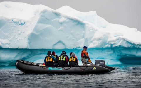 group of travelers in a zodiac skiff looking at a turquoise antarctica icebergy