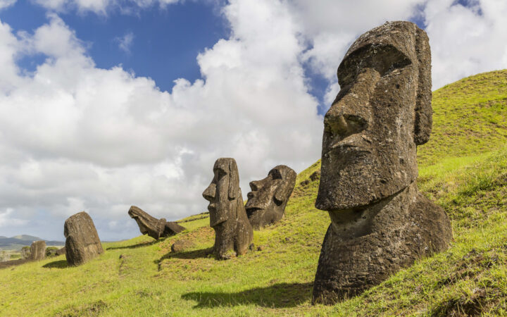 moai statues on easter island chile stand on a grassy hillside with sun an puffy clouds above
