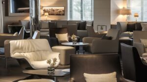 Lounge area aboard Le Soleal grey and white arm chairs and love seats around glass coffee tables, warm lighting on the wall