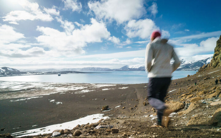 Hiker walking down a trail down to the Antarctic Peninsula with small cruise ship in the backgorund.