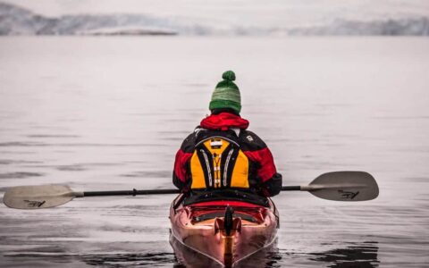 Guest kayaking with beanie with the Antarctic Peninsula in the backgorund