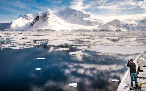 Passenger on the bow deck of the Plancius is taking a picture of a mountain, travel, cruise, polar cruise, expedition cruise, in the polar region.