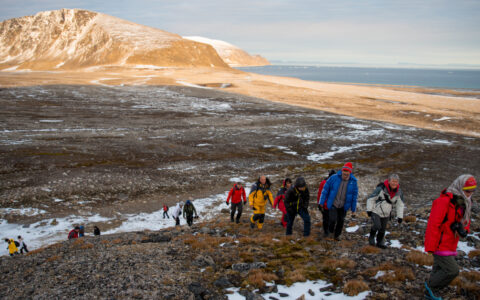 Hikers exploring the arctic landcapes dressed in cold weather gear as the sun sets behind them