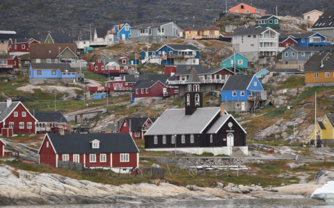 Hearty Arctic homes of different bright colors sit on hillside of tundra in Greenland, seen on a Commandant Charcot cruise.