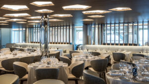 Nuna restaurant with white table cloths & place settings, gray-&-beige seats & posh atmosphere on Le Commandant Charcot ship.