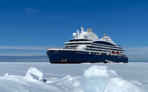 Expedition ship with dark blue hull & white upper decks sits in ice during Le Commandant Charcot Northeast Greenland Voyages.