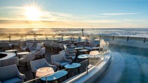 Top deck of Le Commandant Charcot polar ship, with chaise loungers along a semi-circular pool at sunset.