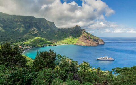 Aerial view of small ship parked in the bay of a lush green island in the Easter Island to Tahiti: Tales of the Pacific cruise.