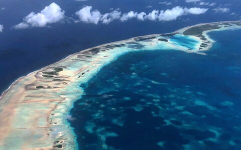 Aerial view of a string of Tahitian islands & coral reef surrounded by turquoise & deep blue water on the Easter Island to Tahiti cruise.