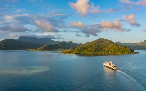 Aerial view of small ship cruising in the bay of a lush green island in the Easter Island to Tahiti: Tales of the Pacific cruise.