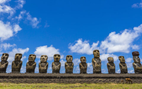 line of moai statues in chile all facing the same direction on a sunny day with clouds above