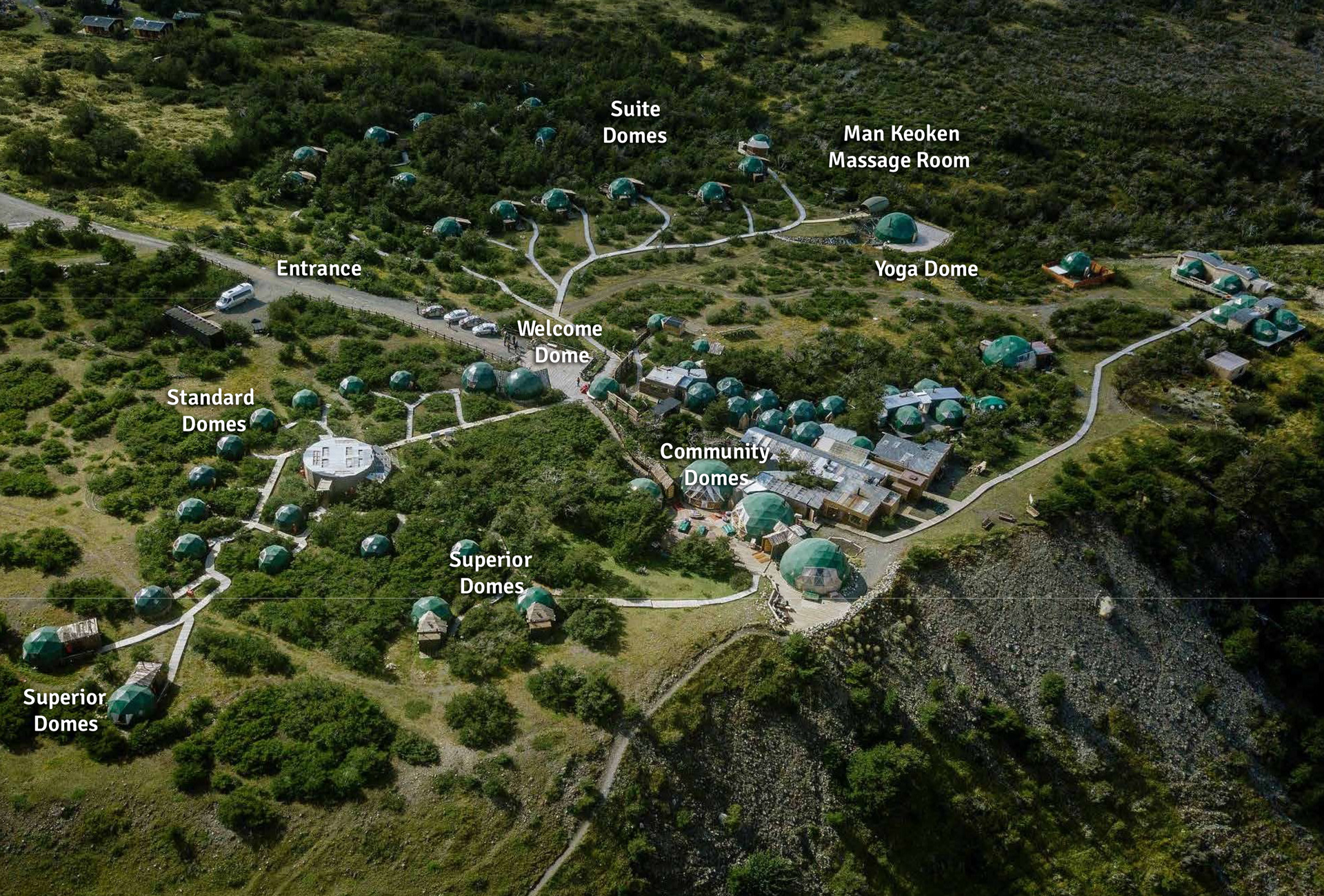Aerial view of EcoCamp Patagonia with multiple teal domed buildings labeled, set in green hills.