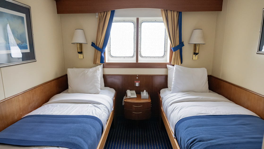 Main Deck Window Twin cabin on G Expedition ship with 2 twin beds in blue & white linens, wood accents & 2 small windows.